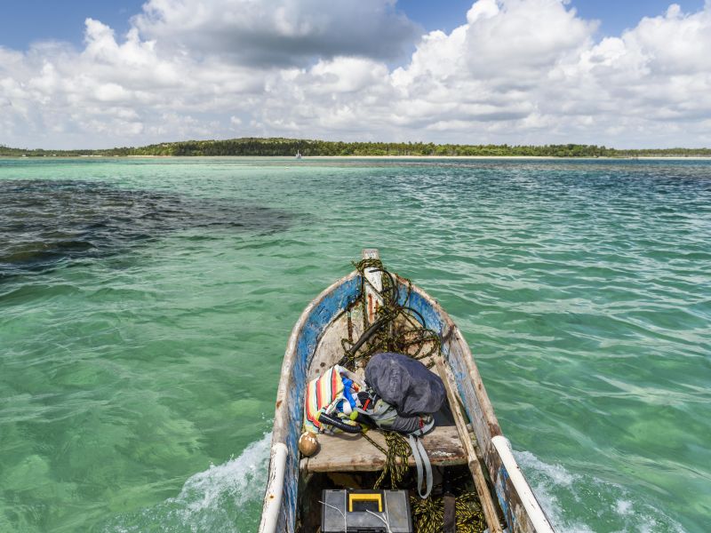 Visão de parte de um barco de pesca navegando no mar esverdeado na Ilha de Boipeba, com a ilha ao fundo