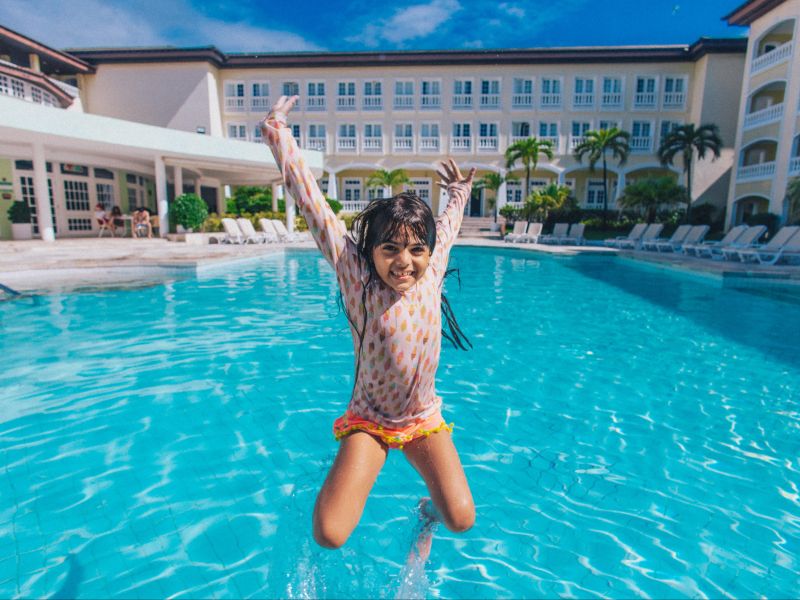 Criança saltando na piscina do Costa do Sauípe Resorts, com o hotel ao fundo