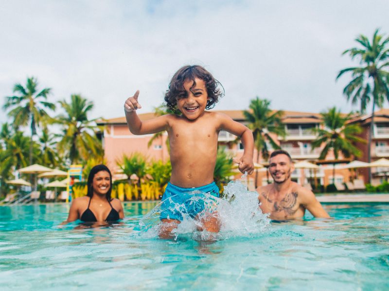 Criança correndo em uma piscina na Costa do Sauípe, com os pais ao fundo