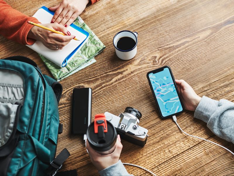 Visão de cima das mãos de pessoas planejando uma viagem com celulares, mapas e câmera 