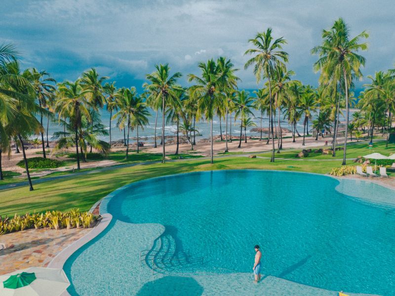 Pessoa no meio de uma piscina com a praia da Costa do Sauípe ao fundo